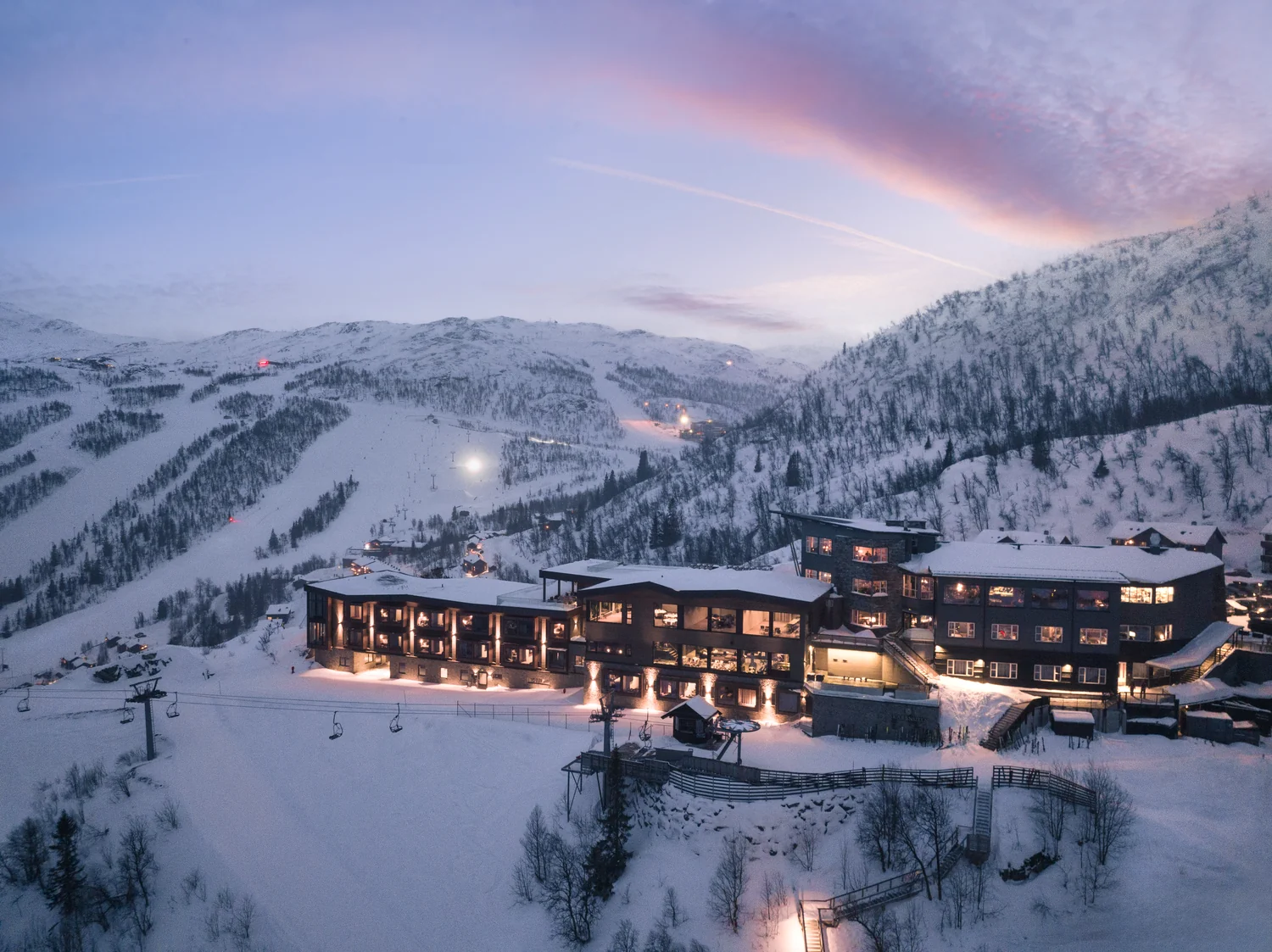 Vinterlig hotell fotografert med drone Hotell i snødekte fjell ved skumring med varme romlys