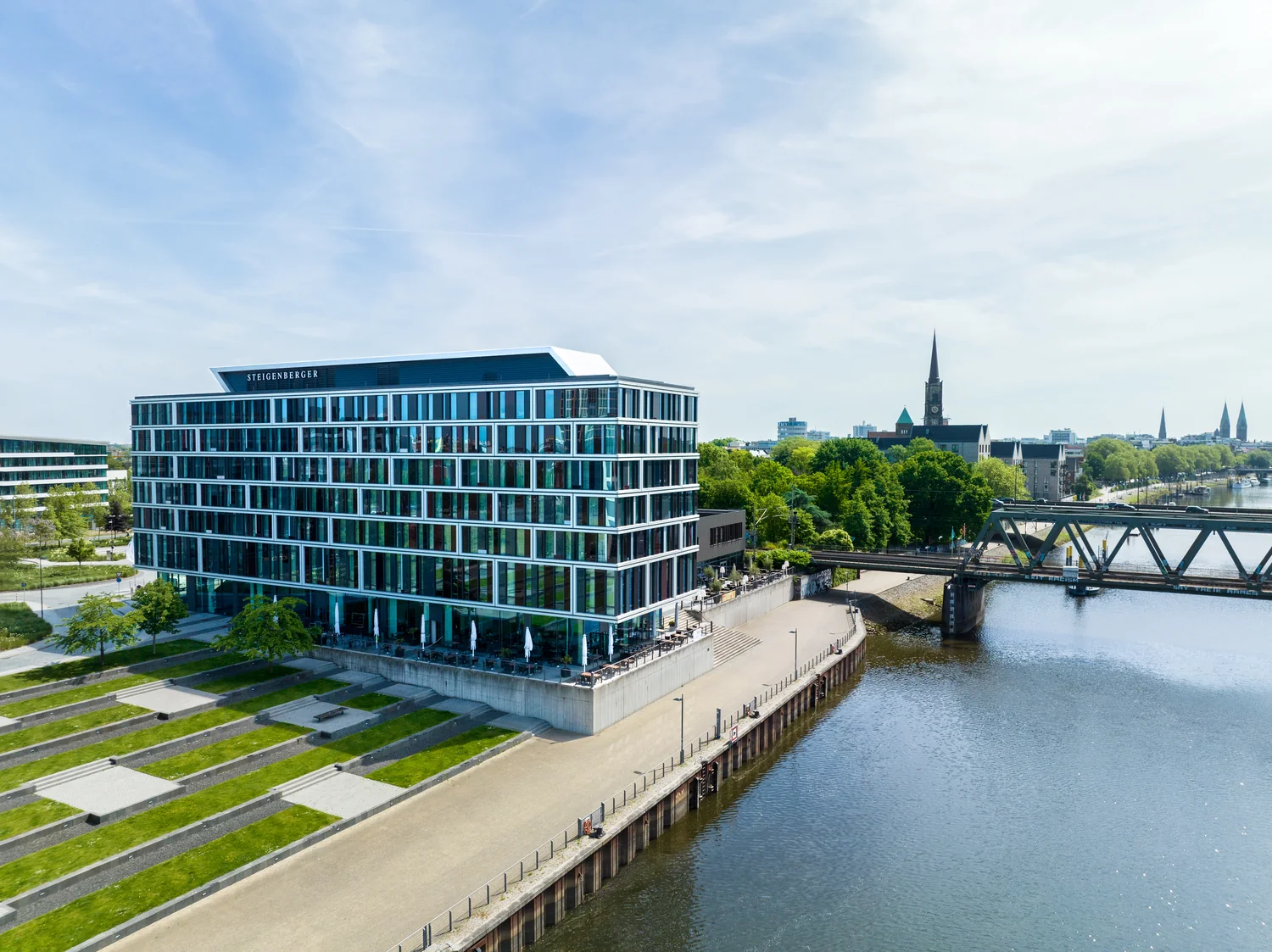 Moderne hotell og omgivelser sett fra luften Dronebilde av moderne hotell ved vannet med utsikt mot elv, bro og by