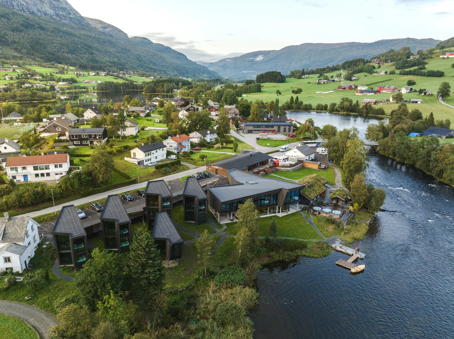 Hotell i landskap med elv og fjell Dronebilde av moderne hotell i naturnært område ved elv og fjell