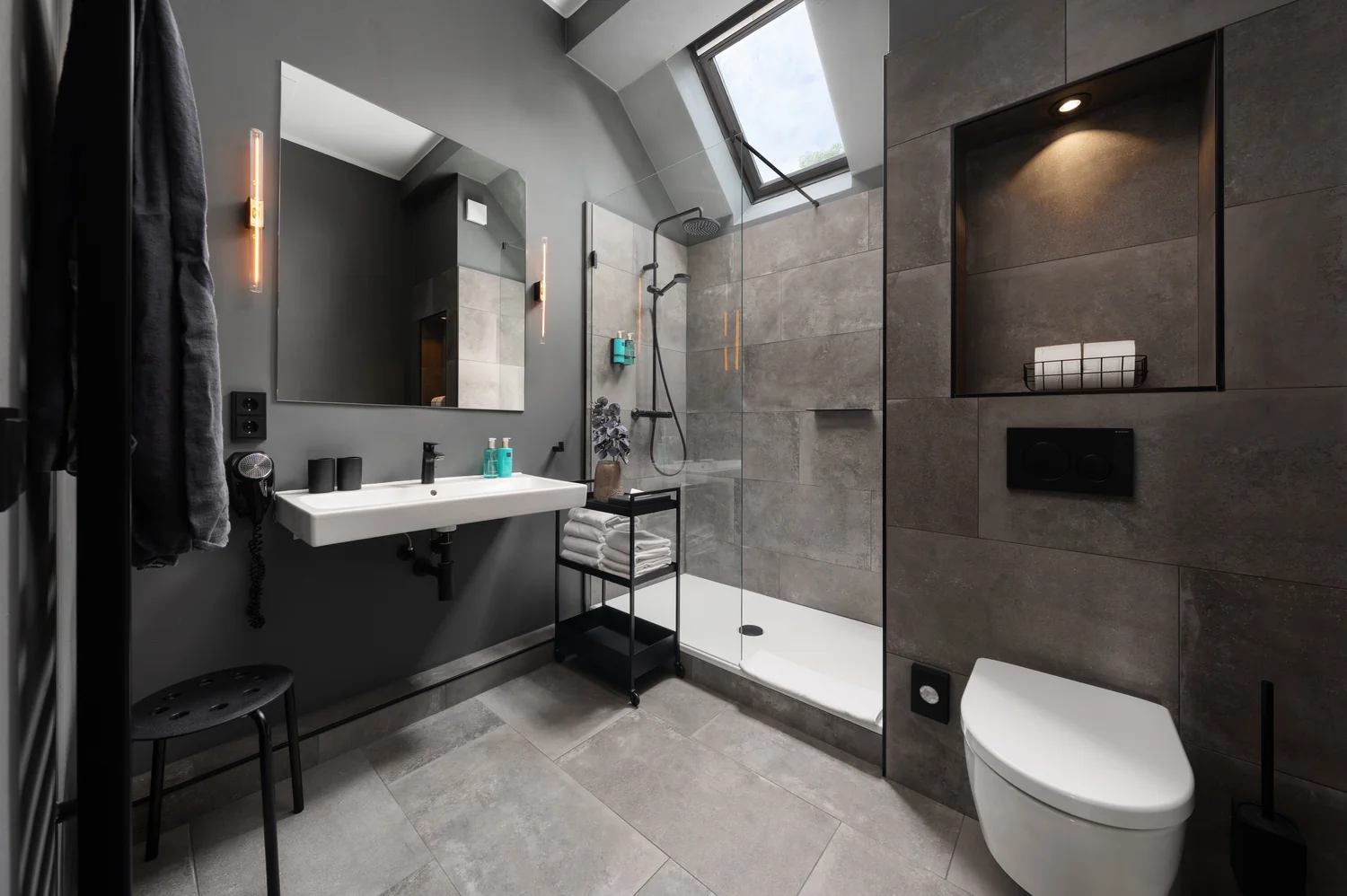 Mørkt hotellbad med gjennomført lyssetting Moderne designbad med mørke fliser, dusj og stemningsfull belysning